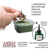 Miniature figure being dipped into a container of green paint with text on how to use Battlefields Basing Glue.